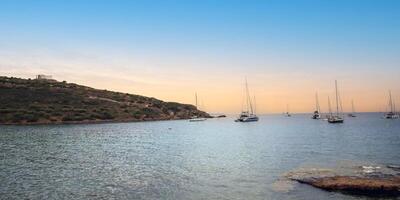 At the Aegean Sea near the Temple of Poseidon in Sounion, Greece, witness a captivating sunset scene adorned with boats surrounding the majestic Poseidon temple photo