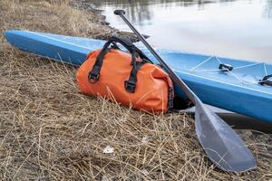 touring stand up paddleboard with a paddle, waterproof duffel and sport watch on a lake shore, early spring in Colorado photo