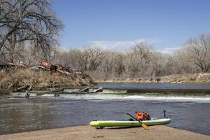 inflatable stand up paddleboard with a paddle, dry bag and action camera on a sandbar below diversion dam, early spring paddling on the South Platte River in Colorado. photo