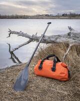 waterproof duffel and stand up paddle on a lake shore photo