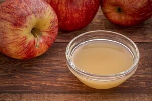 unfiltered, raw apple cider vinegar with mother - a small glass bowl with fresh red apples photo