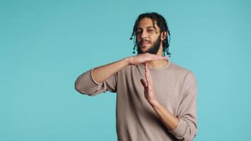 Assertive middle eastern man asking for timeout, doing hand gestures. BIPOC person doing pause sign gesturing, wishing for break, isolated over blue studio background, camera A video