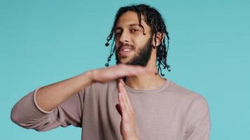 Assertive middle eastern man asking for timeout, doing hand gestures. BIPOC man doing pause sign gesturing, wishing for break, isolated over blue studio background, camera B video