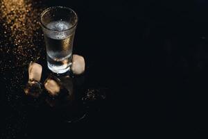 Vodka in shot glasses on black background, iced strong drink in misted glass. photo