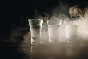 Vodka in shot glasses on black background, iced strong drink in misted glass. photo