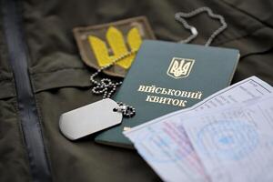 Military token or army ID ticket with mobilization notice lies on green ukrainian military uniform photo
