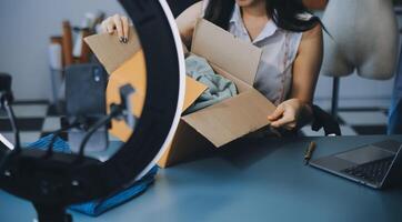 Beautiful asian woman blogger showing bag in front of camera to recording vlog video live streaming at her shop.Business online influencer on social media concept. photo