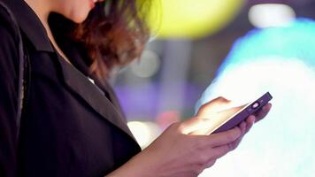 Aziatisch vrouw meerdere rassen mooi. bedrijf vrouw gebruik makend van smartphone Aan een stad straat met neon bokeh lichten schijnend Bij nacht. vrouw op zoek Bij mobiel telefoon wandelen in straat met verlichting Aan aanplakbord. video