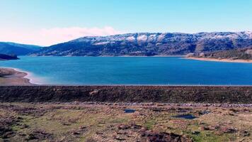 sereno lago con spolverato di neve montagne nel il sfondo, nazionale parco mavrovo nel macedonia, Visualizza a partire dal il superiore, aereo video