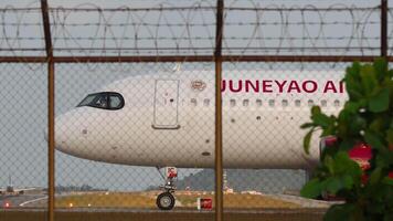 PHUKET, THAILAND - FEBRUARY 16, 2023. Commercial plane Airbus A320, B-321C of Juneyao Airlines taxiing at Phuket airport, side view. Airliner on the runway, view through the fence video