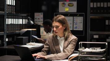 Detective inspector and male police officer investigate in office, examining files and evidence with expertise. Portrait shot of caucasian policewoman cross-checking information on paper with laptop. photo