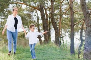 madre y pequeño hijo contento familia. atractivo mamá, niño chico son caminando despreocupado al aire libre verano. padre mujer va en naturaleza juntos con Niño,verano,primavera luz del día,copia espacio. contento familia. foto