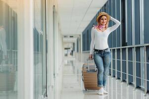 Casually dressed young stylish female traveller checking a departures board at the airport terminal hall in front of check in couters. Flight schedule display blured in the background. Focus on woman. photo