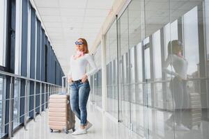 Casually dressed young stylish female traveller checking a departures board at the airport terminal hall in front of check in couters. Flight schedule display blured in the background. Focus on woman. photo