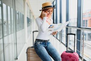 Casually dressed young stylish female traveller checking a departures board at the airport terminal hall in front of check in couters. Flight schedule display blured in the background. Focus on woman. photo