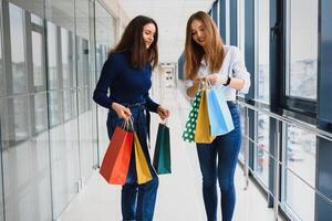 Two girl-friends on shopping walk on shopping centre with bags photo