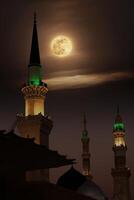 A mosque with the full moon in the sky. Masjid nabi of Medina, mosque at night. Masjid nabi of Medina. Green dome and moon.. photo