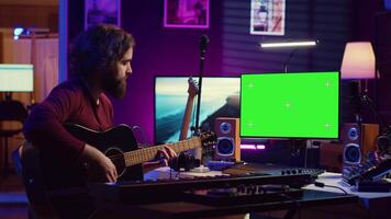 jong artiest spelen zijn gitaar en beoefenen nieuw lied met online zelfstudie, looks Bij computer met groene scherm Scherm. musicus aan het leren nieuw akoestisch instrument akkoorden, huis studio. camera a. video