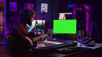 jong artiest spelen zijn gitaar en beoefenen nieuw lied met online zelfstudie, looks Bij computer met groene scherm Scherm. musicus aan het leren nieuw akoestisch instrument akkoorden, huis studio. camera b. video