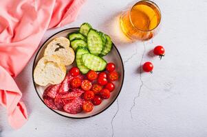 Girl dinner of smoked sausage, cucumbers, cherry tomatoes and buns on a plate top view photo