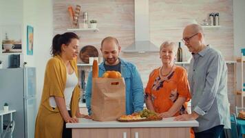 video portret van gelukkig uitgebreid familie glimlachen Bij de camera, zittend in de keuken. mensen in dining kamer in de omgeving van de papper zak met boodschappen op zoek Bij de web cam