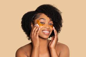 Joyful black woman with golden under-eye patches, skin care routine photo