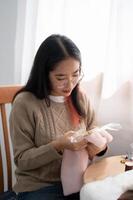 un hermosa asiático mujer es enfoque en coser a mano un modelo en paño en un bordado marco. foto