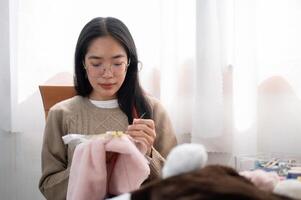 un calma asiático mujer es coser a mano un modelo en un bordado marco, disfrutando su pasatiempo a hogar. foto
