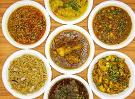 Assorted indian and pakistani spicy food chicken korma, daal mash fry, aloo matar qeema, gobhi gosht, aloo palak and gur chawal served in plate isolated on table top view photo