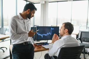 dos hombres comerciantes sentado a escritorio a oficina juntos supervisión cepo datos vela cartas en pantalla analizando precio fluir sonriente alegre teniendo lucro trabajo en equipo concepto foto