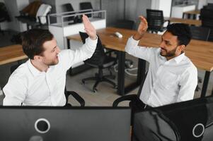 Two men traders sitting at desk at office together monitoring stocks data candle charts on screen analyzing price flow smiling cheerful having profit teamwork concept photo