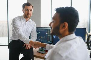 dos hombres comerciantes sentado a escritorio a oficina juntos supervisión cepo datos vela cartas en pantalla analizando precio fluir sonriente alegre teniendo lucro trabajo en equipo concepto foto