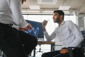 Two men traders sitting at desk at office together monitoring stocks data candle charts on screen analyzing price flow smiling cheerful having profit teamwork concept photo