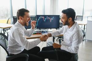 dos hombres comerciantes sentado a escritorio a oficina juntos supervisión cepo datos vela cartas en pantalla analizando precio fluir sonriente alegre teniendo lucro trabajo en equipo concepto foto