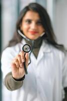 Young Indian medical student at the clinic in practice using a stetoskope in front of camera photo
