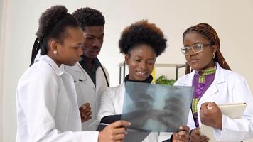 un grupo de cuatro africano americano doctores discutir un radiografía escaneos de un paciente video