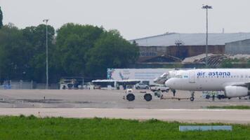 ALMATY, KAZAKHSTAN - MAY 4, 2019. Tractor pulling a passenger aircraft. Airbus A320, P4-KBD of Air Astana at Almaty airport, side view. Airfield on a summer day video