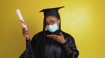 el africano americano hembra graduado estudiante en un protector máscara y con un diploma en mano expresa el gesto de el necesitar a cumplir con cuarentena seguridad medidas. educación concepto video