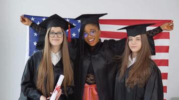 tre donne studenti nel laurea tute e cappelli hold il Stati Uniti d'America bandiera dietro loro portatori. studenti di diverso gare con il Stati Uniti d'America bandiera video