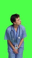 Front view Medical assistant being impatient against greenscreen backdrop, looking around and waiting for patients at consultations. Nurse with health expertise feeling frustrated while she waits. Camera B. video