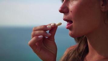 vrouw aan het eten melkachtig amandel noten. een jong Kaukasisch vrouw aan het eten vers amandel na ochtend- geschiktheid yoga in de buurt zee. gezond veganistisch voedsel. langzaam beweging video