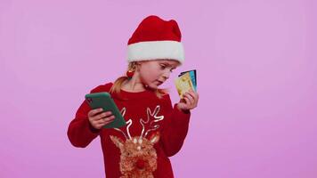 Child girl in Christmas sweateruse mobile cell phone, plastic credit bank cards, win, calebrate, wow video