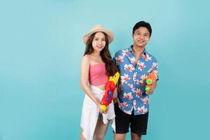 Portrait of Young Asian couple in summer outfits and holding water gun isolated on blue background with copy space. Songkran festiva. photo