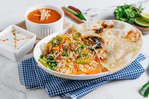 vegetable biryani with raita and sauce in a dish isolated on napkin side view on grey background famous indian and pakistani food photo