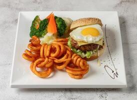 súper shiok carne de vaca hamburguesa con soleado lado arriba huevo, Rizado papas fritas y ensalada servido en plato aislado gris antecedentes parte superior ver Singapur rápido comida foto