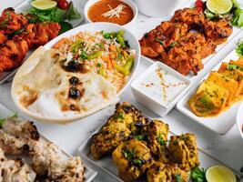 Assorted famous indian and pakistani food table vegetable biryani, Butter Chicken, paneer Chicken Tikka boti kebab, lime, Kali Mirchi, tomato sauce, raita, roti, salad, top view on grey background photo