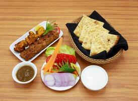 Spicy bbq platter meal with chicken tikka boti, beef seekh kabab, salad, roghni naan, raita and chilli sauce served in a dish isolated on grey background side view of indian, pakistani food photo