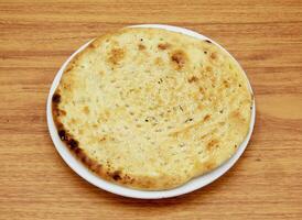 Roghni naan or nan, nun, roti, tandoori, chapati, pita, bread served in a dish isolated on wooden table side view of indian, pakistani food photo