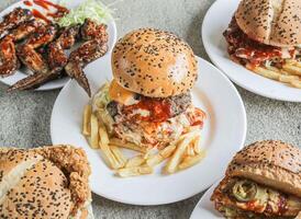 Assorted fastfood Bbq chicken buffalo wings classic beef, chicken, jalapeno and mushroom burgers served in a dish isolated on grey background side view of fast food photo