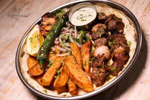 Tikka boti rub kebab with salad, wedges, lemon and dip served in dish isolated on background top view of arabic food photo